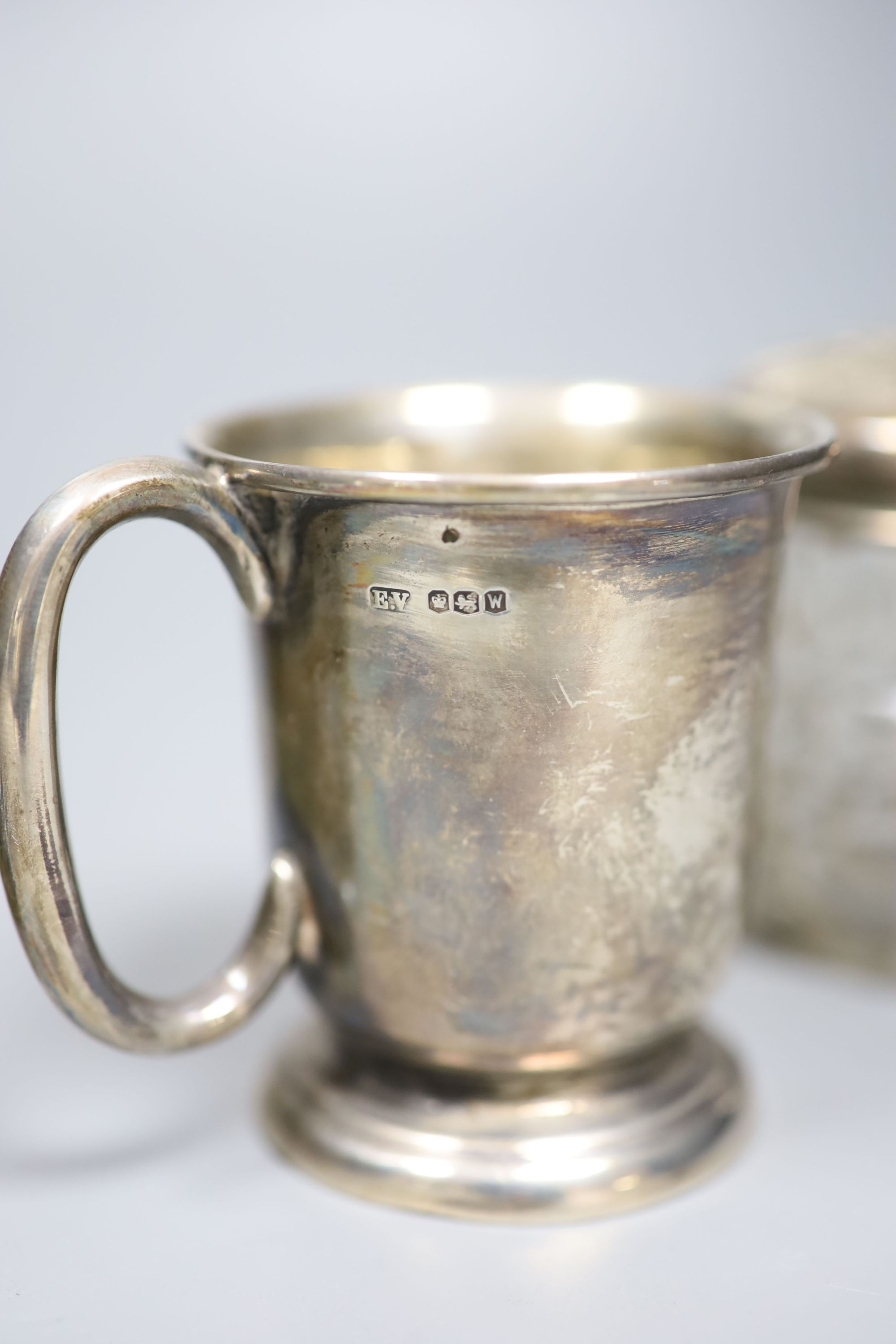 A George VI silver christening mug, a silver mounted cigarette box, a silver mounted scent bottle and toilet jar.